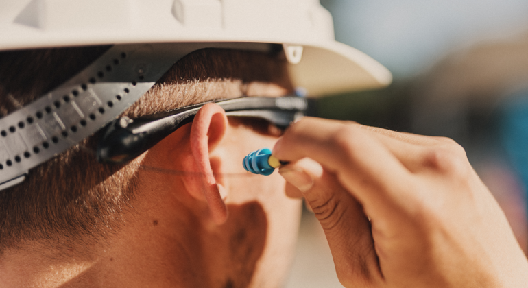 A worker wearing SoundShield safety glasses inserting the earplugs into his ear